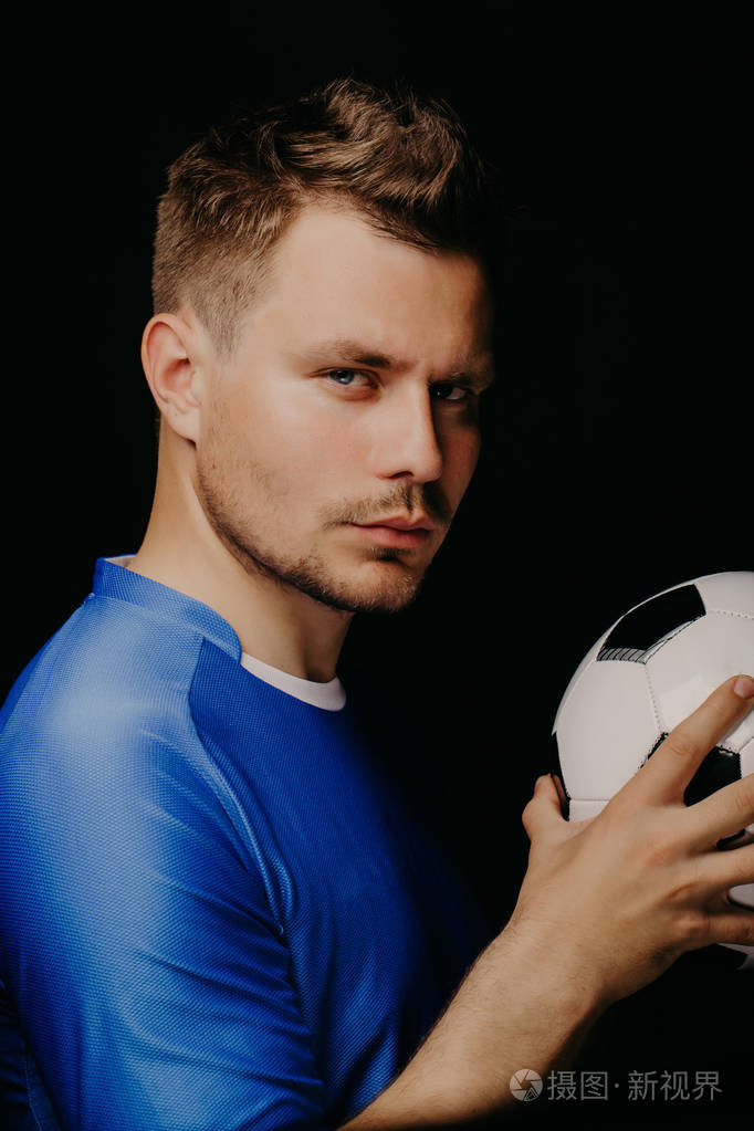 年轻英俊足球运动员的特写肖像在黑暗背景下摆出的足球
