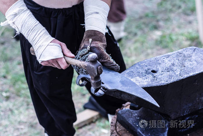 中世纪铁匠的手是用锤子工具在铁砧上制造斧头的过程近距离选择性聚焦
