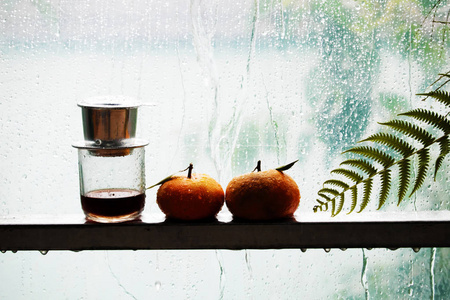 雨背景对比颜色橙色和青色的两种橙色水果咖啡杯蕨叶,雨天和窗户上的