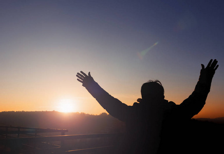 草地音乐会情绪健康概念:日落草地背景下的人举手的剪影照片