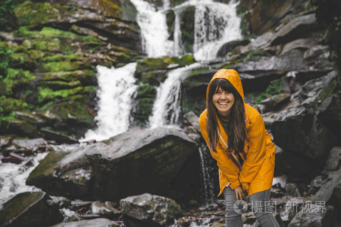 女人穿着黄色雨衣，看着瀑布。 徒步旅行概念