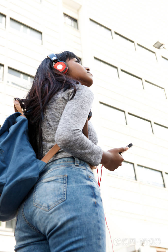 印度年轻女性手持手机和耳机站在城市的侧面画像