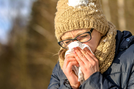 打喷嚏的女人用纸巾吹鼻子. 冬天室外感冒和流感的生病妇女.