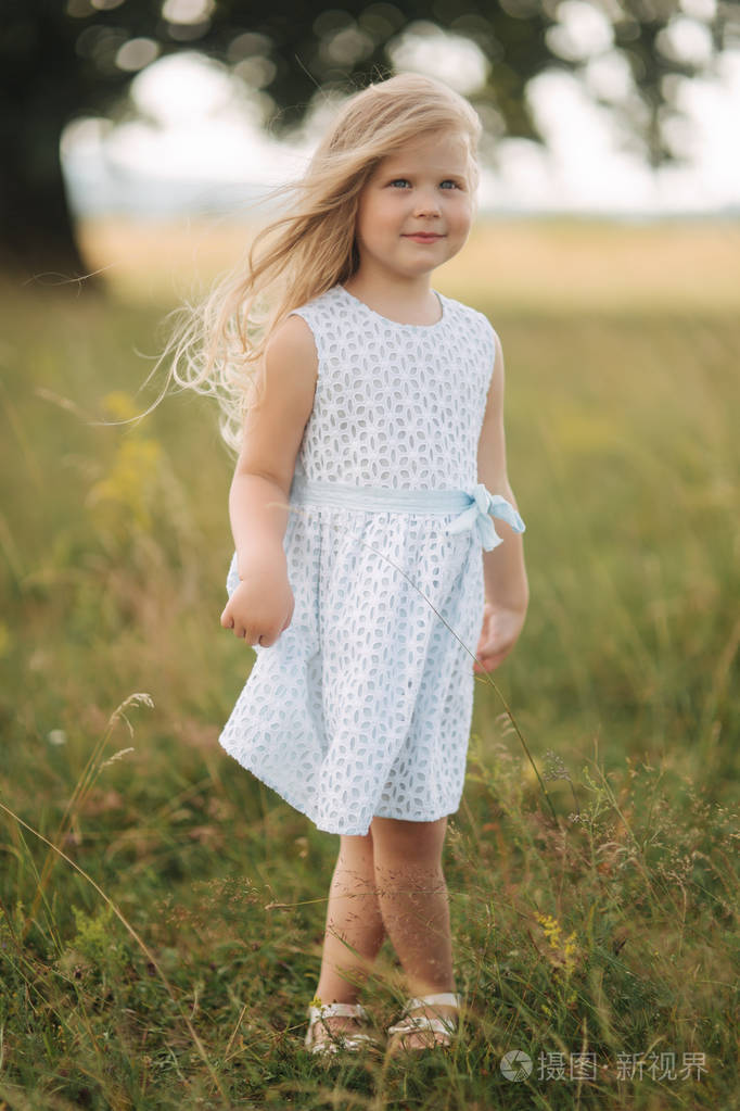 小女孩在天空蓝色礼服站立在领域在大树前面