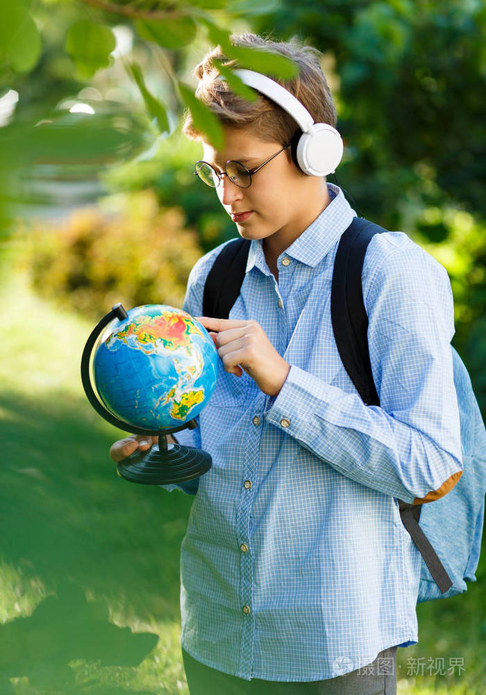 可爱的小男孩穿着蓝色衬衫,背包和工作簿,手里拿着地球仪,在公园的