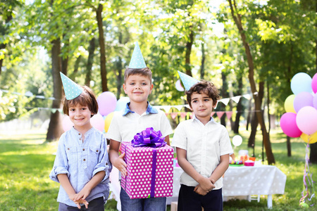 可爱的小男孩带着礼品盒,他的朋友在户外参加生日聚会照片