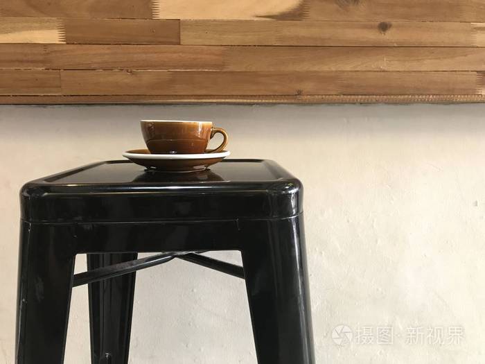 棕色咖啡杯，带茶托的黑色金属酒吧凳子，带有天然木咖啡吧和白色背景的咖啡店。
