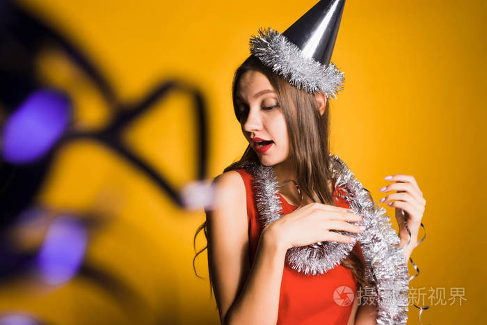 滑稽的年轻女孩在红色礼服庆祝新年, 在她的头一顶帽子, 一个好心情