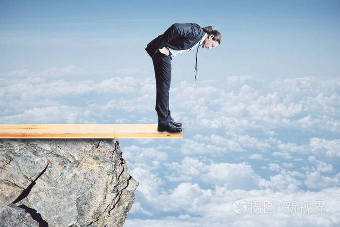 风险和危险概念从悬崖往下看的年轻商人天空背景