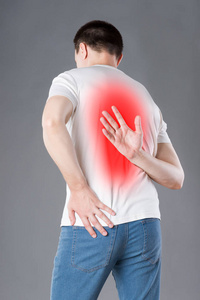 背部疼痛,男人在灰色背景下背痛,疼痛区域以红色突出照片