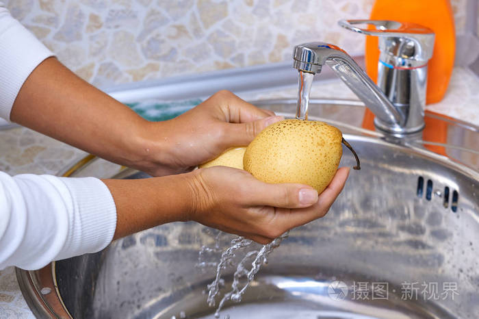 女人用手洗水果梨在厨房的水流下