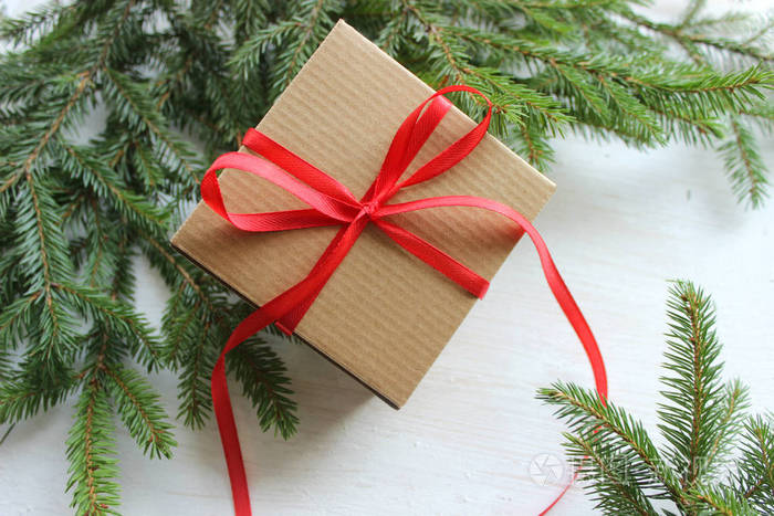 一个白色木制背景礼盒上的绿色冷杉树枝框架，上面有红色缎带圣诞卡。 复制顶部视图