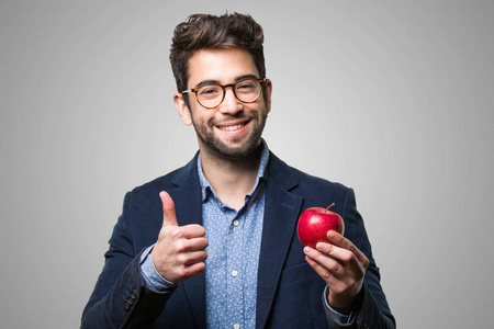在灰色背景下拿着苹果的年轻人做了个好手势照片