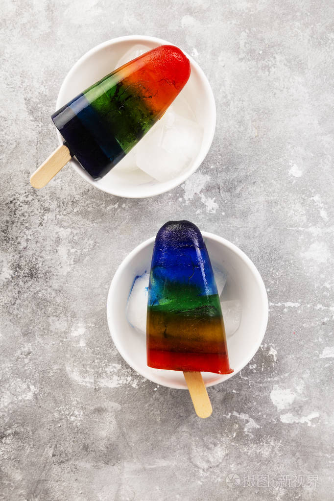 彩虹彩色冰淇淋冰棒与木棒在白色碗在灰色背景上面的风景食物背景