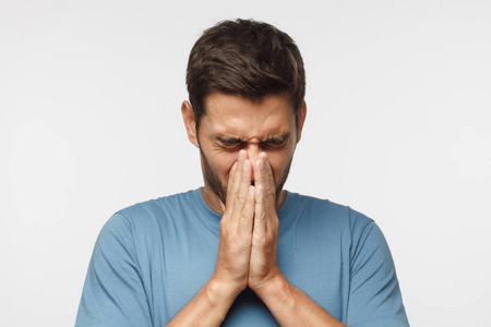 生病的年轻人捂脸,双手打喷嚏,灰色背景孤立照片