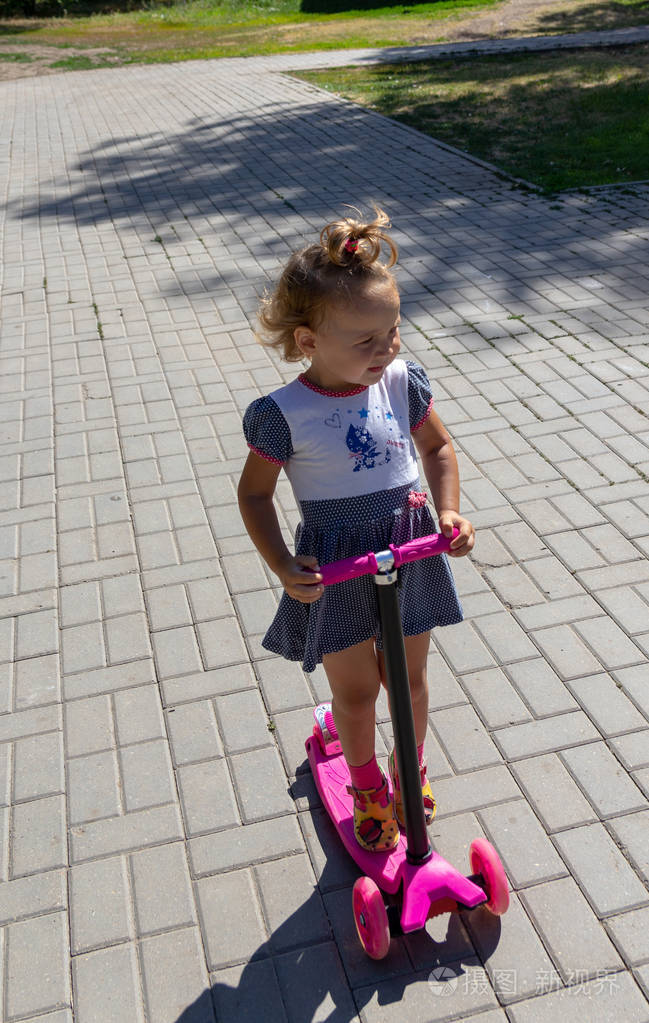 可爱的孩子在夏日阳光明媚的日子里巧妙地在粉红色的两轮滑板车上溜冰