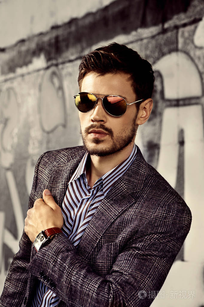 戴墨镜的时髦男人,在涂鸦墙上摆着时髦的夹克照片-正版商用图片1si1st