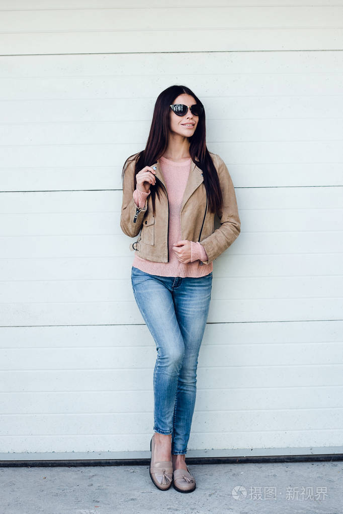 照片 完美的休闲风格. 戴着墨镜,调整外套,站在户外微笑的年轻美女.