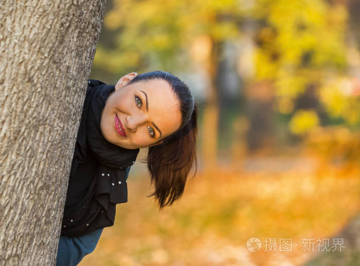 在一个美丽的秋天,幸福的女人躲在一棵树后面.