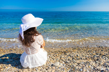 一位年轻的美女,穿着白色连衣裙,坐在海滩上,看着大海的形象,复制了一