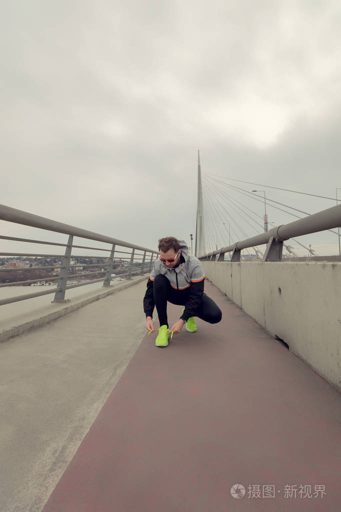 男人在一座大桥上系跑鞋。