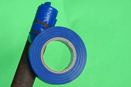 绿色缠绕一条蓝色的带子缠绕在绿色背景上生锈的棕色棍子上照片