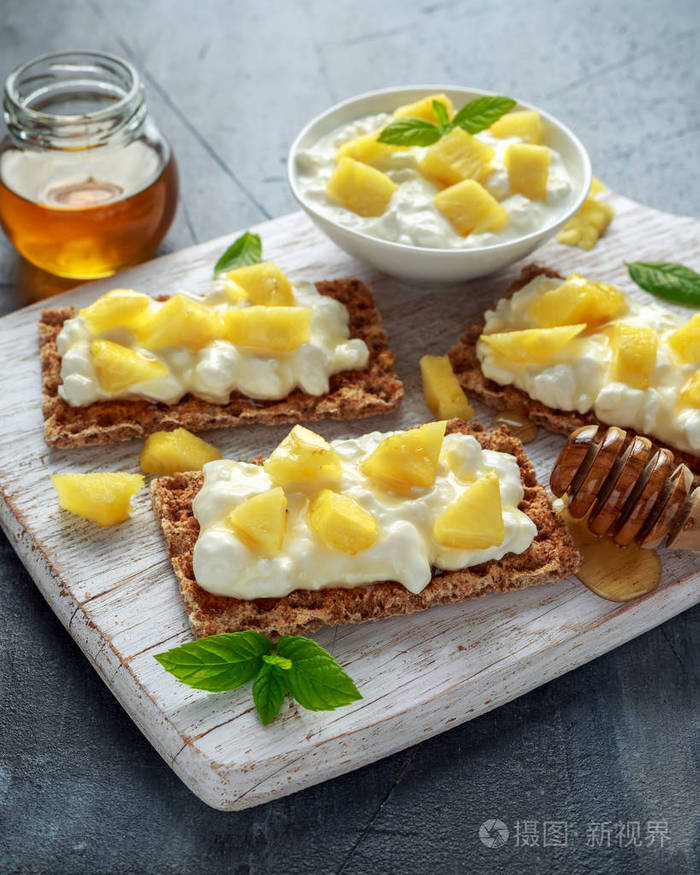 自制薄脆烤面包, 带干酪, 菠萝和蜂蜜在白色木板上