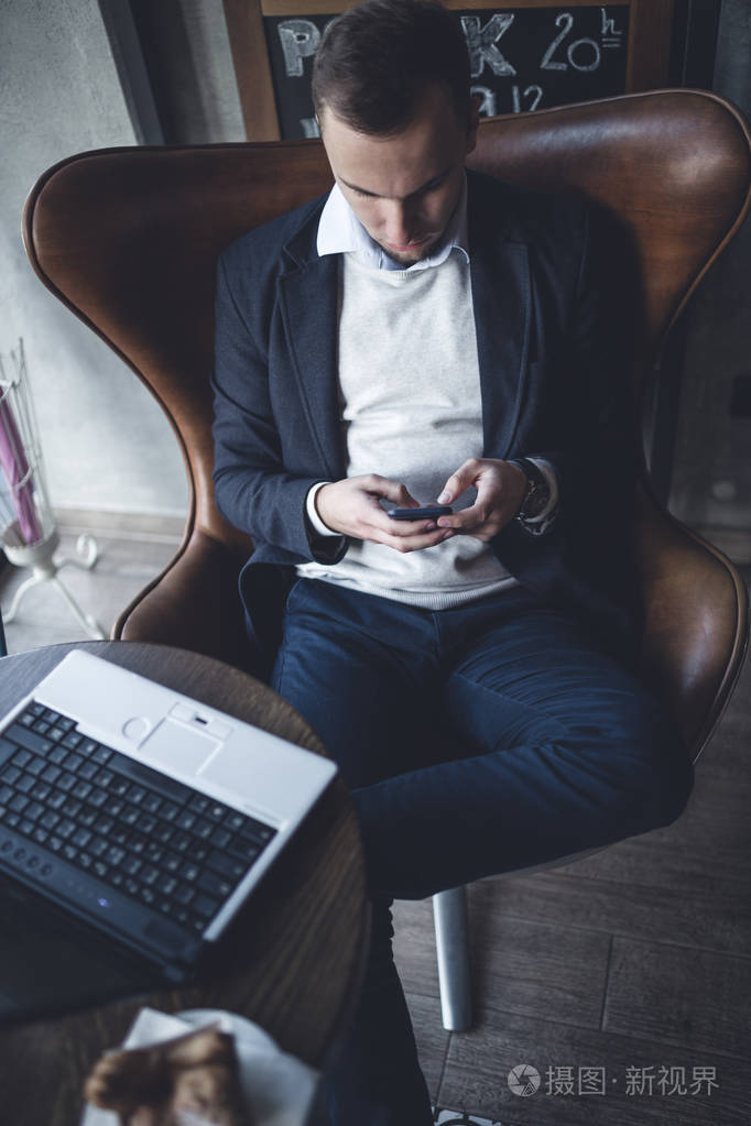 年轻的现代和积极的商人坐在咖啡馆里，用笔记本手机和平板电脑做他的工作。