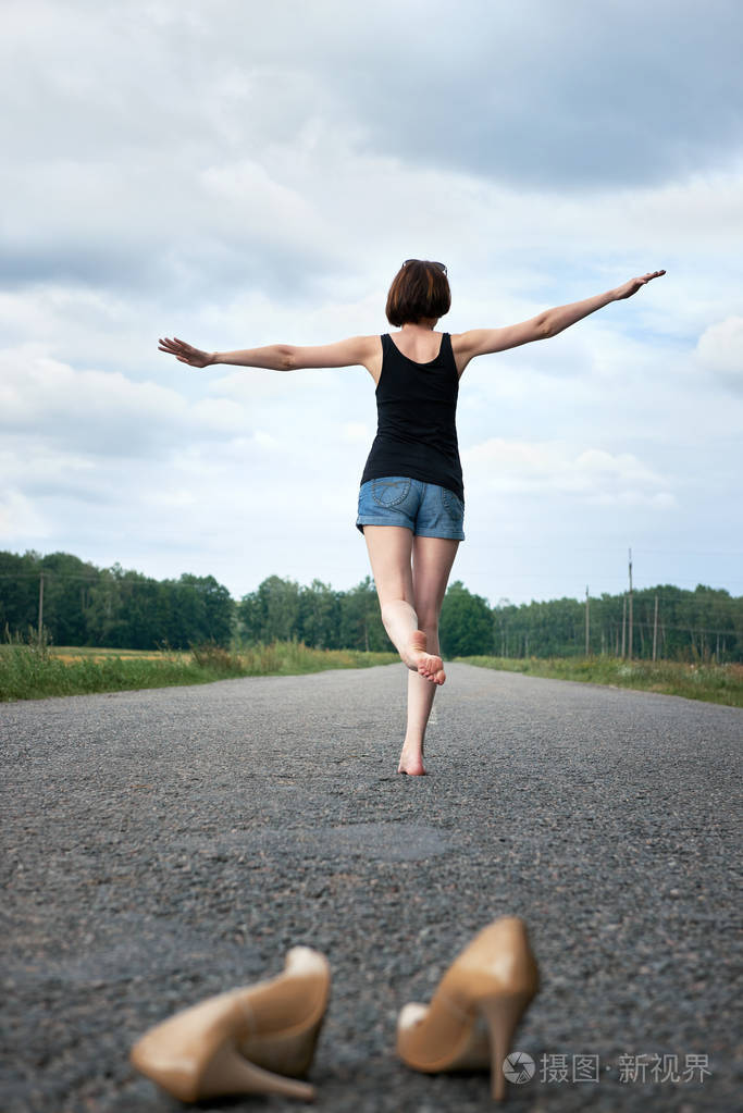年轻的女孩赤脚走在路上她把鞋子落在路上忘记了夏天和旅行的概念