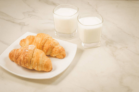 早餐,牛角面包和牛奶/剪刀在盘子里,眼镜牛奶在白色大理石桌子上.