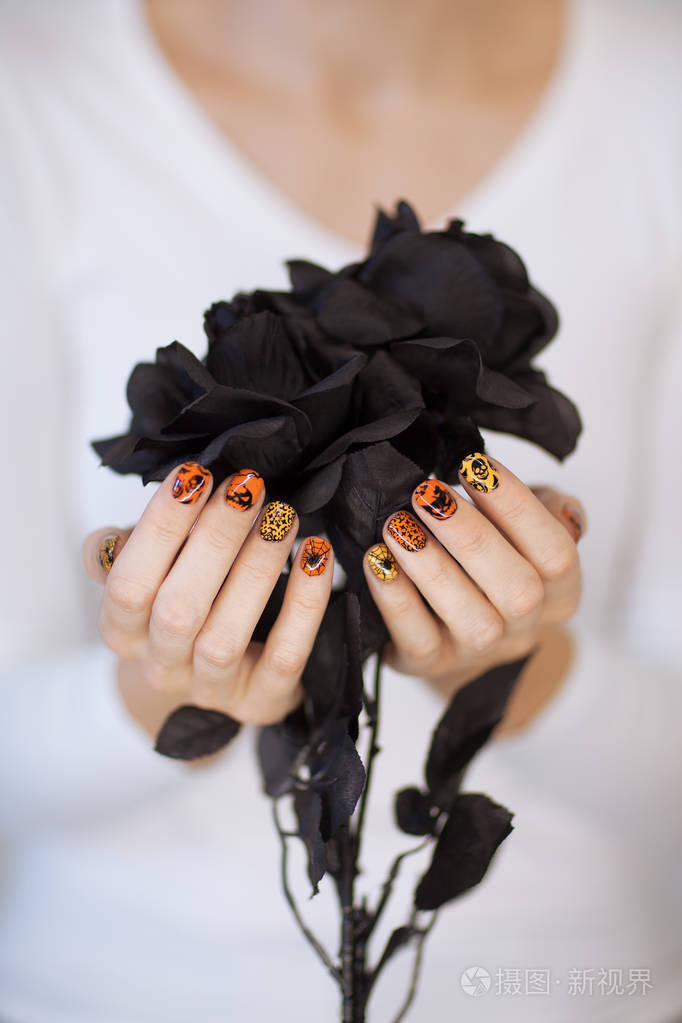 美丽的女人手拿着可爱的万圣节指甲油拿着黑色玫瑰