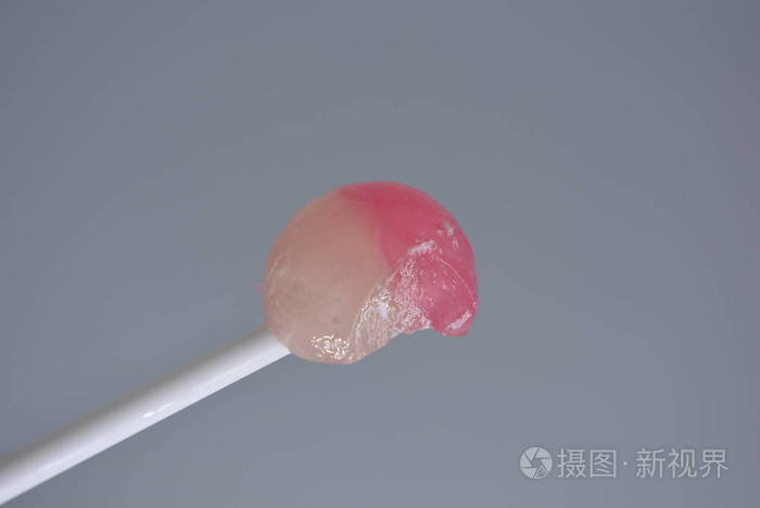 白色塑料棒上的一颗白色和粉红色的白色塑料棒上的一颗被咬的甜糖果