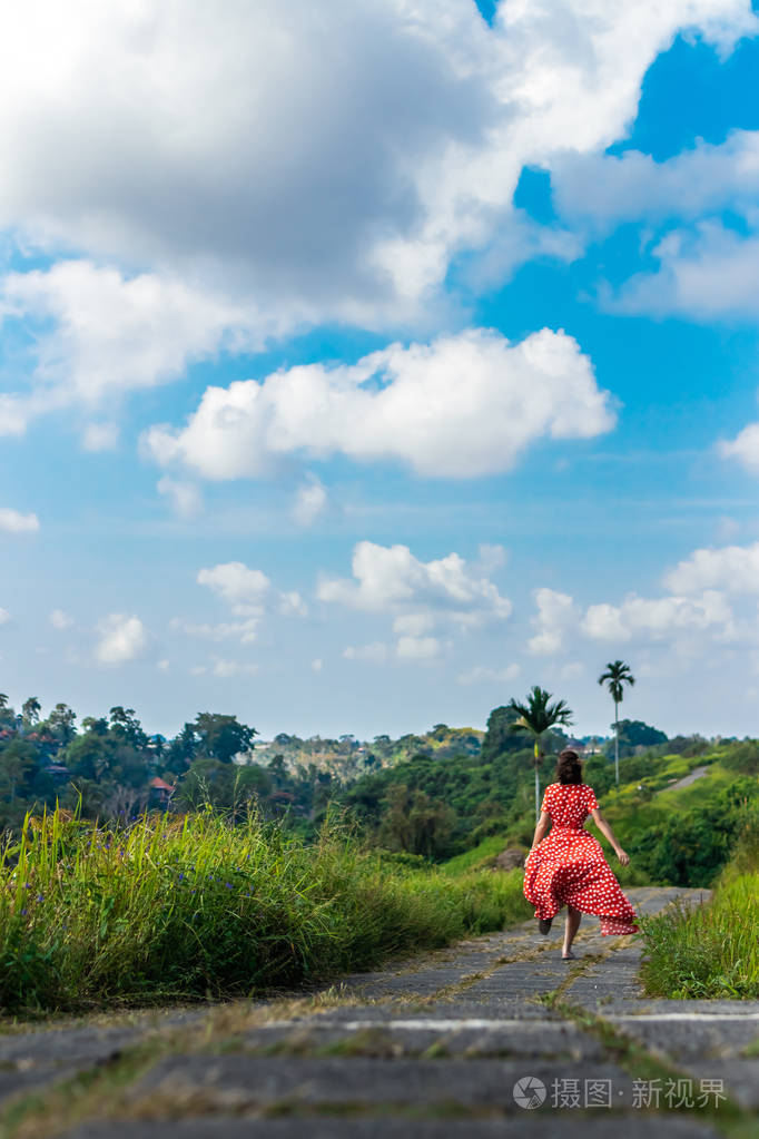 年轻的女人穿着一件孤独的红色连衣裙在热带雨林小径