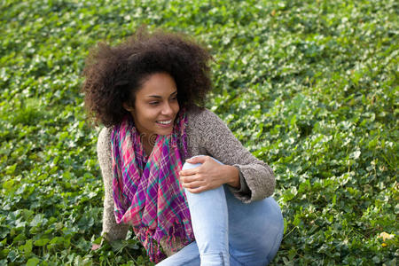 开朗的年轻女人坐在户外的草地上