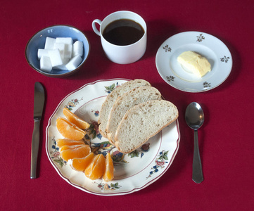 早餐配备咖啡，面包，黄油和橙色楔形在红色桌布上