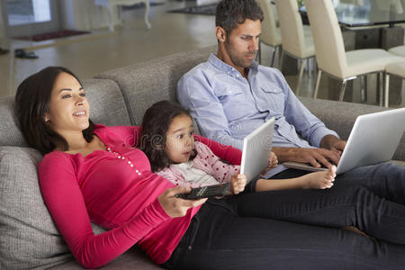 家庭在沙发上带笔记本电脑和数字平板电脑看电视