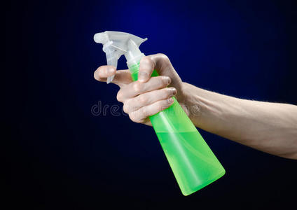 清洁房子和清洁主题男人的手拿着一个绿色的喷雾瓶，在深蓝色的背景上清洁