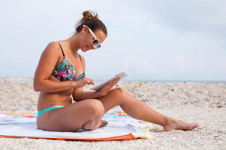美丽的女人坐在海滩上用她的平板电脑