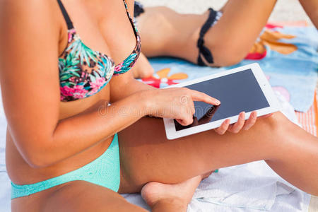 美丽的女人坐在海滩上用她的平板电脑