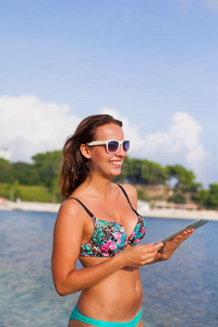美丽的女人站在海滩上拿着平板电脑