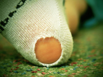 脏的地毯孩子穿着脏袜子,鞋跟上有洞. 腿在绿色地毯上照片