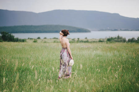 美丽的嬉皮士女人在绿色的田野上摆姿势，背景上有山。