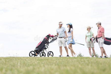 朋友们在高尔夫球场对着晴朗的天空散步时交流