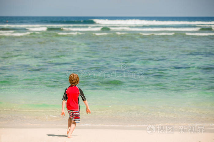 可爱的7岁男孩穿着红色的鲁西西游泳衣在热带海滩与白沙和绿色的海洋