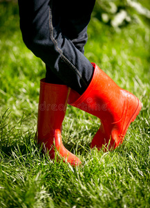 穿着红色橡胶靴的女孩在新鲜的绿色草地上摆姿势的特写
