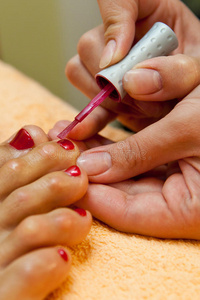 美容师照顾女性客户的脚，给她做足部美容和涂红指甲。