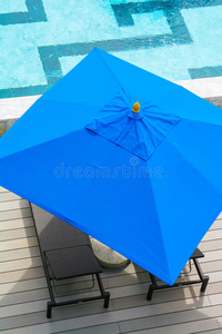 海滩椅子和蓝色雨伞在游泳池旁边
