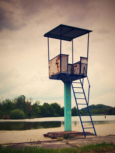 一座古老的白色生锈的金属救生塔，湖边沙滩上有一把椅子。