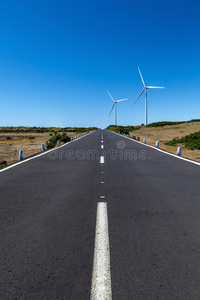 一条笔直的道路，有两个风力涡轮机，覆盖着蓝天