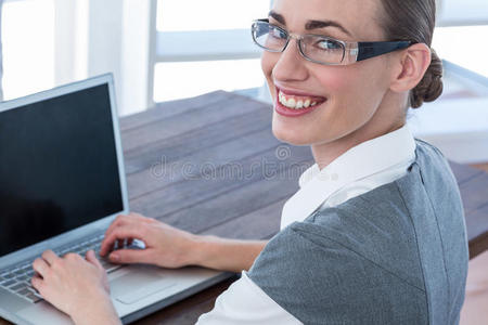 女商人带着眼镜看着相机，用笔记本电脑